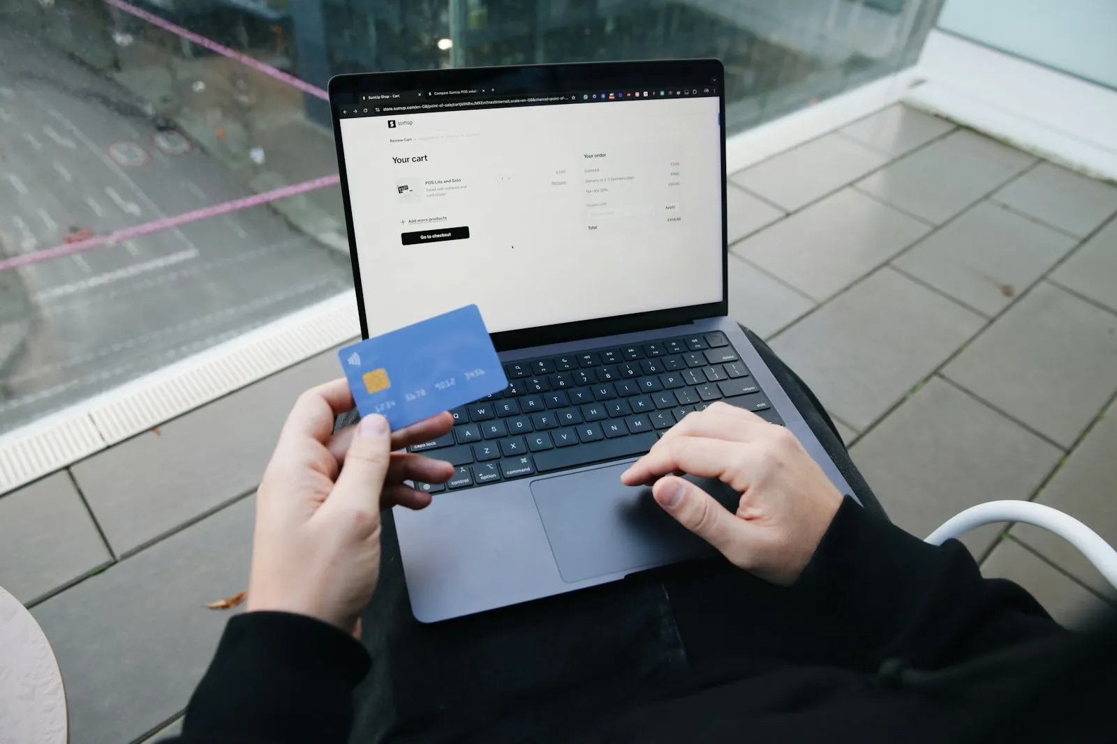 Person sitzt mit Laptop und Kreditkarte und kauft online ein
